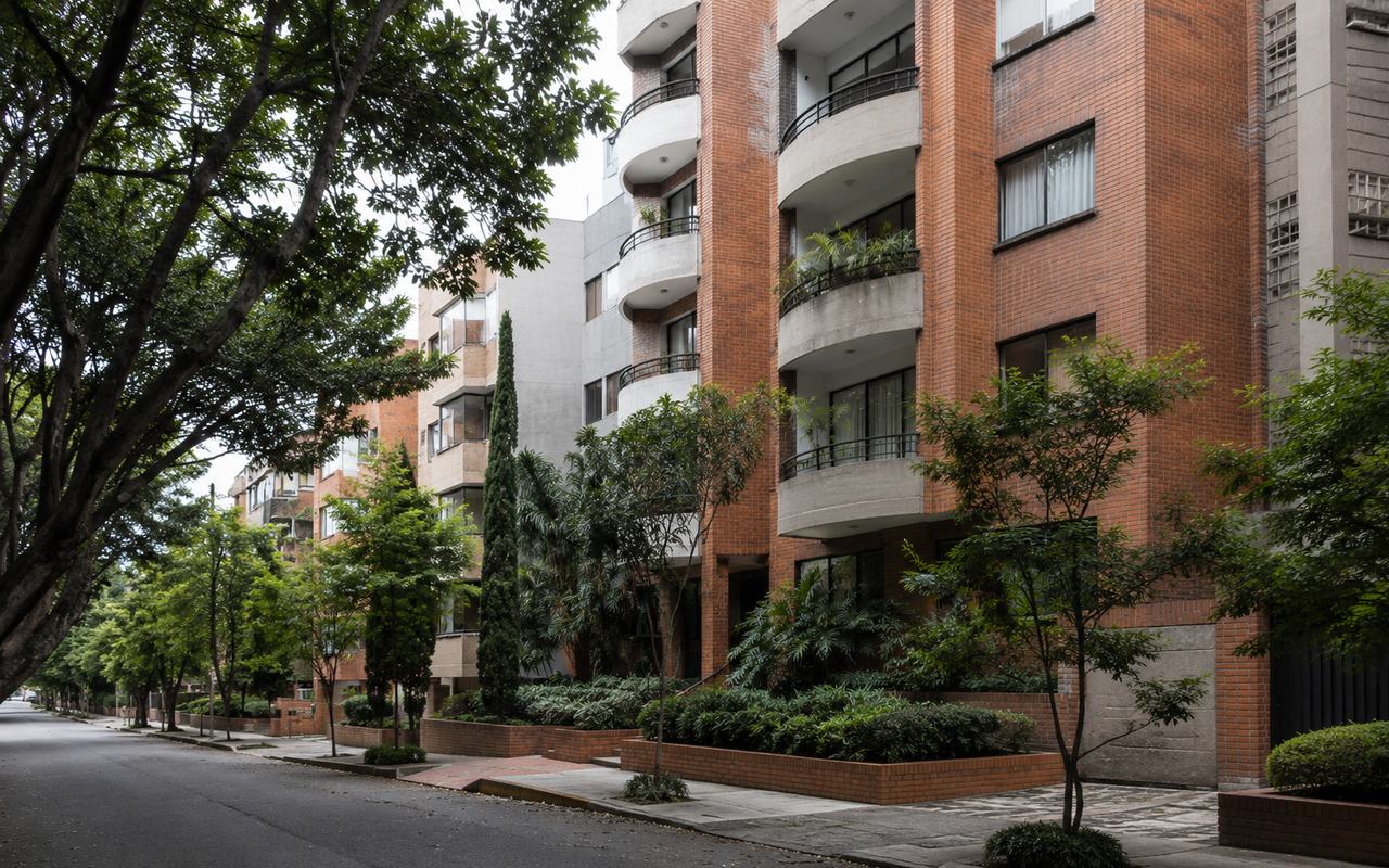 A quiet residential street in Laureles, Medellín, lined with mid-rise brick apartment buildings and mature trees.